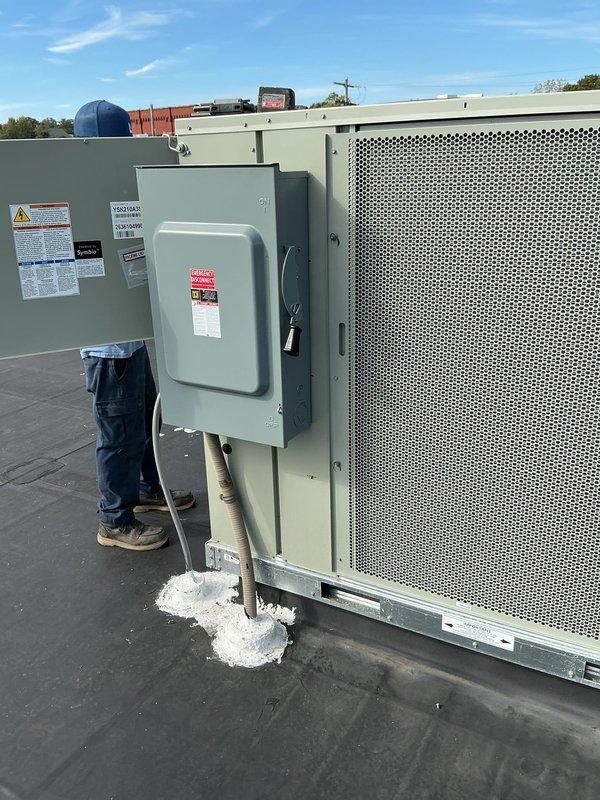 Completed installation of a Trane 17.5-ton rooftop unit on a commercial building with proper mounting, electrical disconnect, and weatherproofing. The RTU was secured to the roof structure with support pads and mounting brackets, with all penetrations sealed appropriately. Unit was positioned, leveled, and verified operational with all safety labels and specifications clearly visible on the equipment.