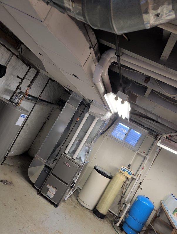 Completed furnace retrofit installation in mechanical room. Removed existing heating unit and installed new gray metal furnace with proper ductwork connections to existing HVAC system. Ensured all supply and return air ducts were properly sealed and secured to new unit. Verified clearances around equipment meet manufacturer specifications and local code requirements. Tested system operation and confirmed proper airflow throughout distribution system.