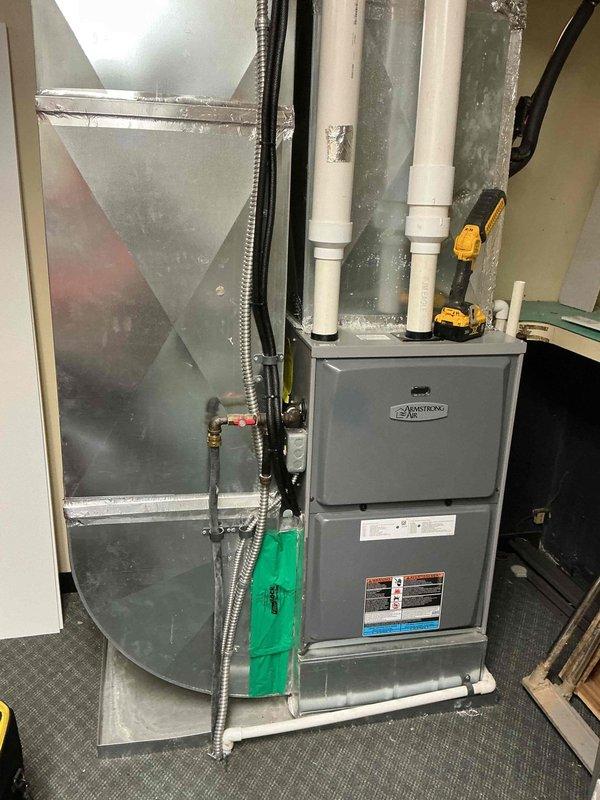 Performed scheduled commercial heating maintenance on an Armstrong Air upright gas furnace, inspecting the cabinet, flue and condensate piping, gas line with shutoff valve, and connected supply ductwork. Noted heavy condensation on the galvanized duct surface with a measured surface temperature of 55.8°F, along with peeling foil tape at a duct seam, indicating a need for insulation and seam sealing to prevent moisture accumulation and potential damage. Recommend re-sealing the duct seams and insulating the affected ductwork.