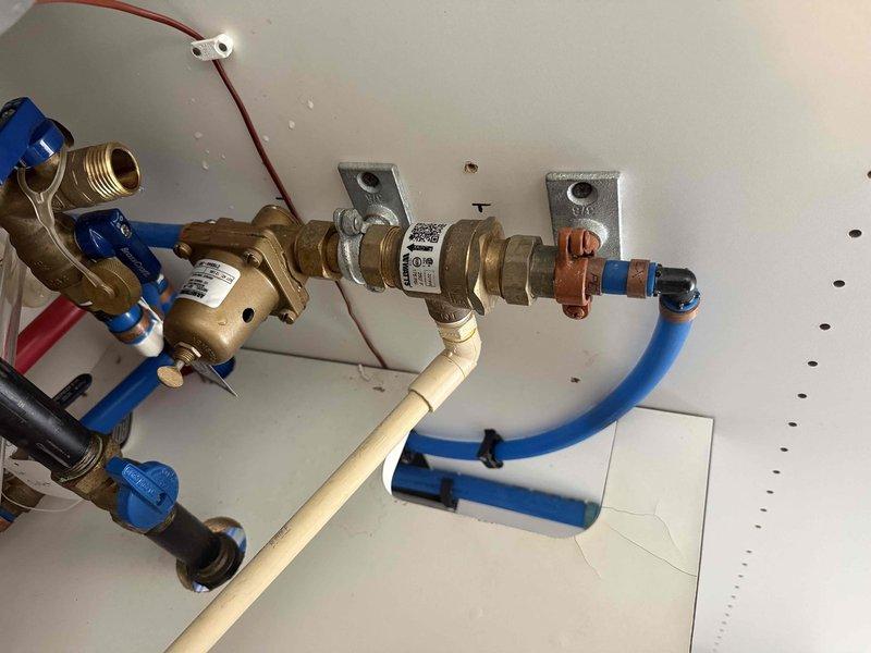 Inspected the reported leaking pressure gauge at the plumbing manifold assembly and verified the brass pressure-reducing valve and inline fittings. Identified moisture at the gauge and adjacent brass fittings, with a hairline crack in the panel edge near the lower cutout. Documented the assembly, confirmed no active leaks, corrosion, or damage at the manifold, PEX lines, or filter housing, and recommended gauge replacement to restore proper pressure monitoring.