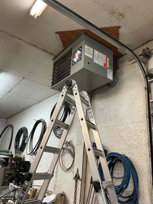 Performed scheduled maintenance on a ceiling-suspended Reznor gas-fired unit heater during a recurring commercial heating contract visit, accessing the unit via ladder to inspect the cabinet, louvers, flue/vent connection to the ceiling penetration, and electrical conduit. Visual inspection found no evidence of rust, frost, or physical damage, and the unit was left in serviceable condition.