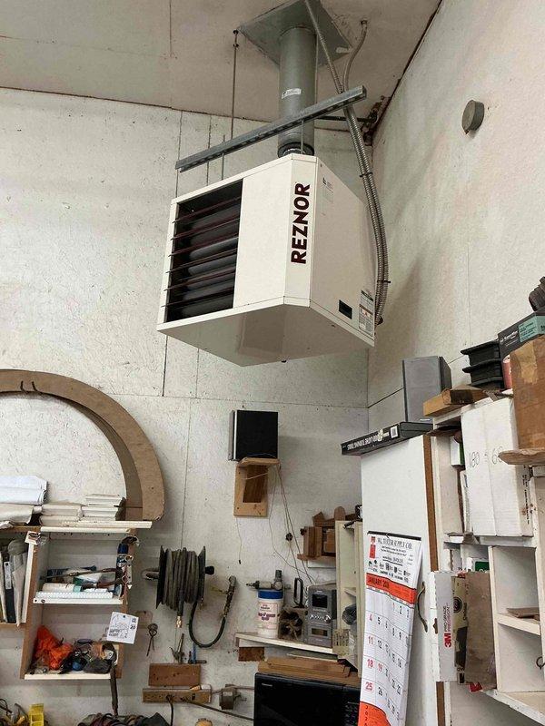Performed scheduled maintenance on a ceiling-suspended Reznor gas-fired unit heater during a recurring commercial heating contract visit, accessing the unit via ladder to inspect the cabinet, louvers, flue/vent connection to the ceiling penetration, and electrical conduit. Visual inspection found no evidence of rust, frost, or physical damage, and the unit was left in serviceable condition.