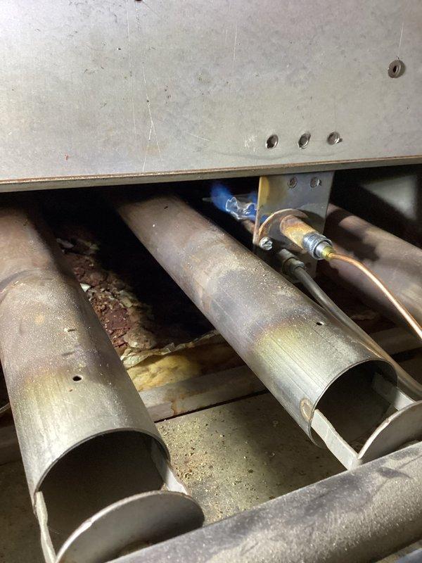 Performed diagnostic evaluation on 30-year-old boiler system responding to recurring issue from previous fall service. Inspected interior components including heat exchanger tubes showing signs of wear and weathering, and examined connection points where copper supply lines attach to the main system. Utilized specialized probe tool to assess operational parameters and system integrity in utility area.