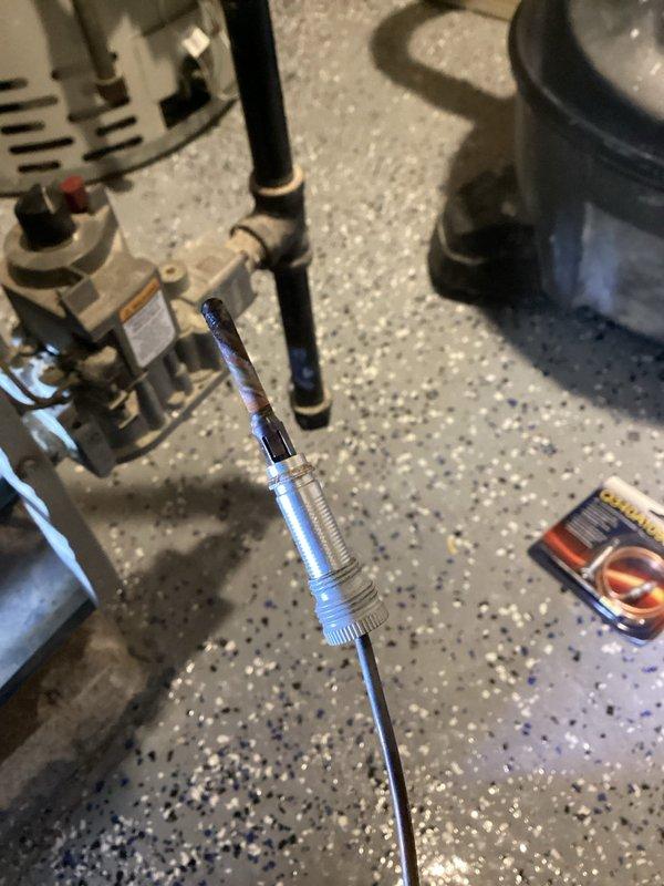 Performed diagnostic evaluation on 30-year-old boiler system responding to recurring issue from previous fall service. Inspected interior components including heat exchanger tubes showing signs of wear and weathering, and examined connection points where copper supply lines attach to the main system. Utilized specialized probe tool to assess operational parameters and system integrity in utility area.