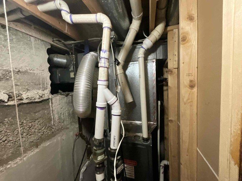 Conducted full system estimate for replacement of aging 17-year-old HVAC equipment with new 2-stage furnace and air conditioner. Inspection revealed existing installation in basement utility area with complex PVC drainage/ventilation network and current furnace showing signs of age-related wear. Photographs documented current system configuration and installation constraints for proper sizing and placement of recommended replacement equipment.