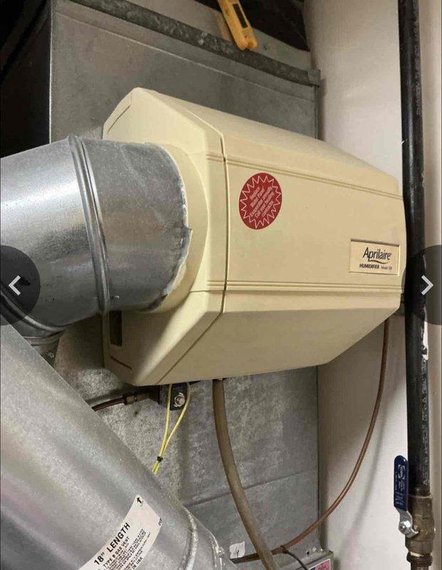 Performed assessment of 14-15 year old furnace system located at rear of property. Documented existing installation including Aprilaire 700M humidifier mounted to ductwork and connected to water supply. System evaluation indicated replacement would be more cost-effective than continued repairs given the unit's age and condition.