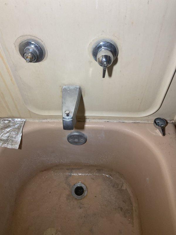 Conducted plumbing estimate for bathroom fixtures showing significant wear. Assessed wall-mounted hot and cold faucet handles in both bathtub/shower and sink areas that were loose and require replacement. Documented water staining on surrounding surfaces and mineral deposits around drain areas, indicating ongoing issues with the current fixtures.