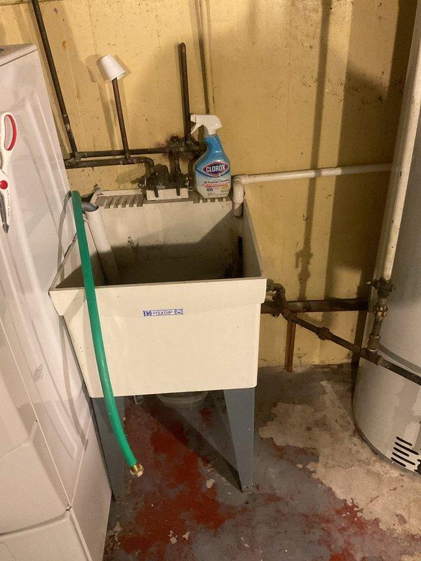 Completed comprehensive plumbing inspection following water heater installation. Identified and documented leaking basement utility sink with corroded supply line fittings and floor staining indicating ongoing water damage. Assessed upstairs bathroom fixtures, noting severely corroded chrome shower valve assembly, escutcheon plate, and tub spout with significant mineral deposits and water staining requiring drain clearing service.