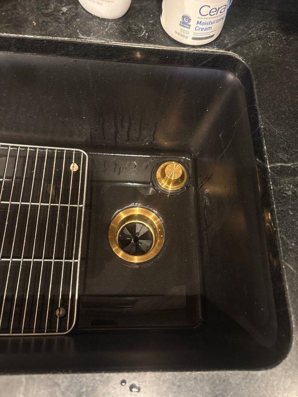 Removed and replaced two garbage disposal units under kitchen sink with black composite basin and brass fixtures. Verified proper drainage operation and tested water flow through both disposal drains to ensure leak-free connections and optimal functionality.
