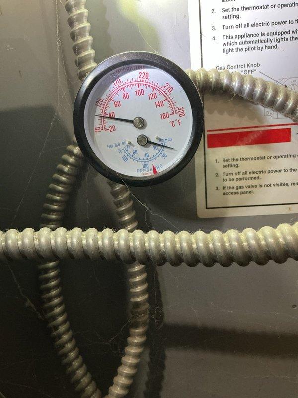 Responded to boiler leak complaint and performed diagnostic inspection. Upon arrival, found active water seepage from boiler system requiring immediate attention. Observed pressure gauge reading at zero position and noted brass drain valve assembly with collection bucket in place beneath unit showing signs of mineral deposits and water discharge. Identified leak source at lower boiler connection point. Completed call-of-the-week (COTW) service evaluation, documented system conditions with photographic evidence, and provided assessment findings. Unit requires follow-up repair to address leaking component and restore proper system operation.