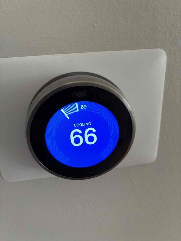 Completed comprehensive air conditioning maintenance inspection under preventative maintenance agreement. Serviced outdoor condensing unit located on side of house with easy access, performed standard cleaning and operational testing. Verified system cooling performance with Nest thermostat displaying 66°F setpoint while actively cooling from 69°F ambient temperature. Inspected electrical disconnect and exterior components, documented equipment condition with photos showing normal weathering and operational status.