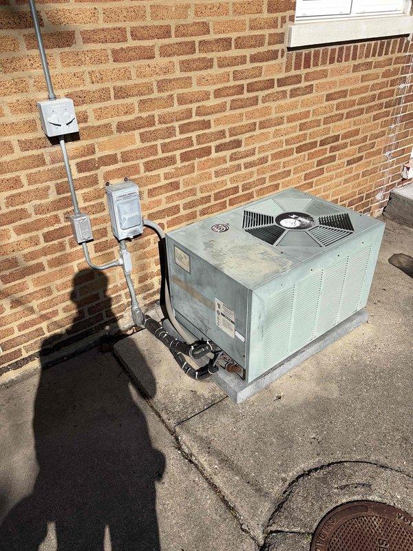 Conducted on-site evaluation of existing cooling system for replacement estimate. Assessed outdoor condensing unit mounted on concrete pad against exterior brick wall, documenting current equipment condition, electrical connections including disconnect switch and junction boxes, and proper clearances. Inspected attic space to evaluate ductwork routing, structural access points, and existing PVC condensate drain line installation to determine requirements for new system installation and any necessary modifications to accommodate replacement equipment.