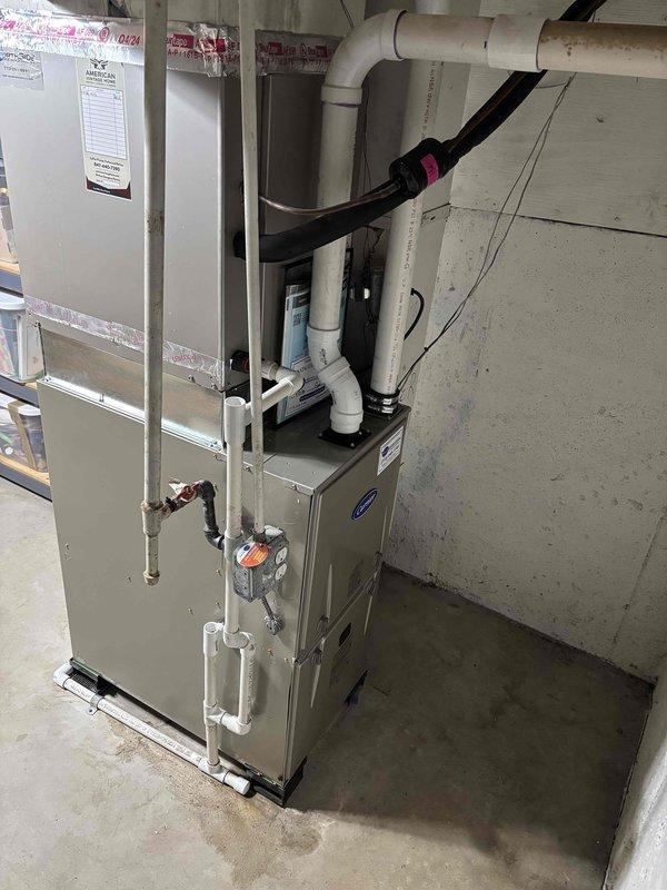 Completed full furnace replacement in residential basement utility area. Removed existing heating unit and installed new beige/tan furnace system with accompanying HVAC components, ensuring proper placement on concrete floor against block wall foundation. Configured all necessary white PVC venting and drainage piping with appropriate routing through ceiling joists, including vertical and horizontal runs with proper elbow joints for code-compliant exhaust and condensate management. Secured black flexible refrigerant lines and insulated ductwork using appropriate fasteners and support straps. Connected all electrical wiring through existing wall-mounted junction boxes and installed proper conduit for system power supply. Verified all manufacturer specifications were met during installation, confirmed proper clearances around equipment, and tested system operation to ensure optimal heating performance and safety compliance.