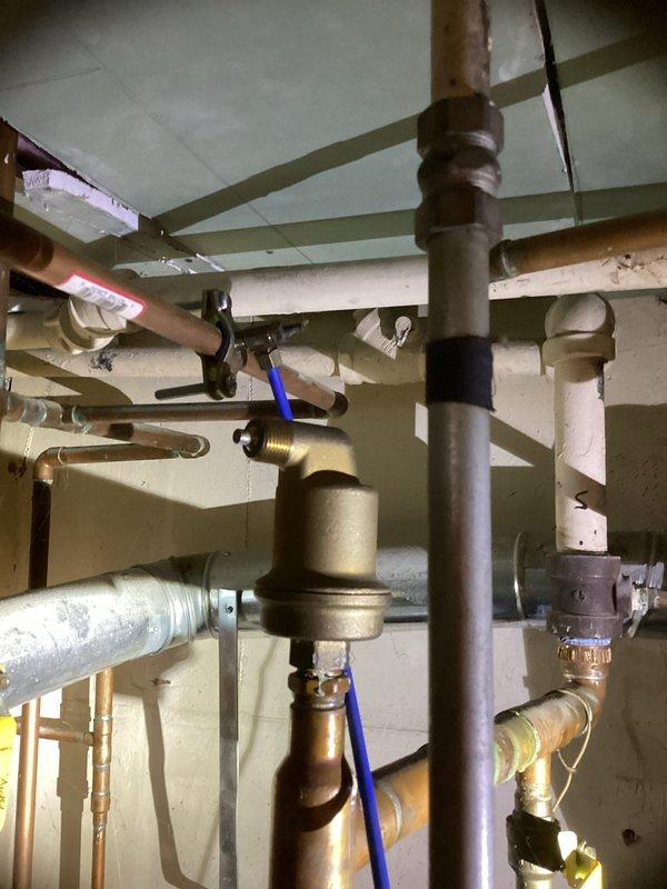 Provided estimate for water heater replacement in extremely confined mechanical space with approximately 6-inch clearance access. Installation will require navigating complex existing plumbing infrastructure including copper supply lines, PVC drainage, and multiple valves and fittings in tight overhead configuration beneath floor joists with acoustic tile ceiling system.