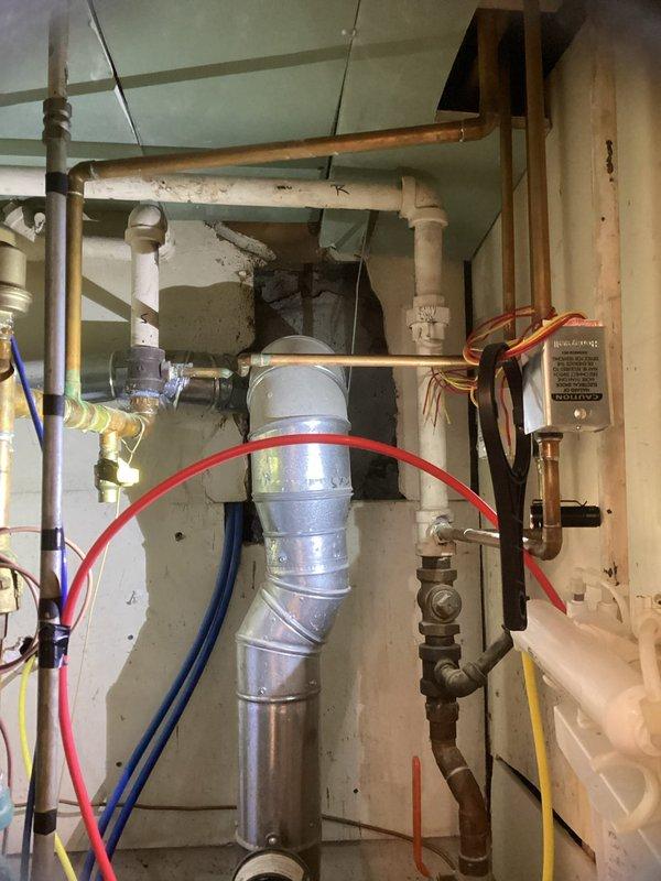 Provided estimate for water heater replacement in extremely confined mechanical space with approximately 6-inch clearance access. Installation will require navigating complex existing plumbing infrastructure including copper supply lines, PVC drainage, and multiple valves and fittings in tight overhead configuration beneath floor joists with acoustic tile ceiling system.