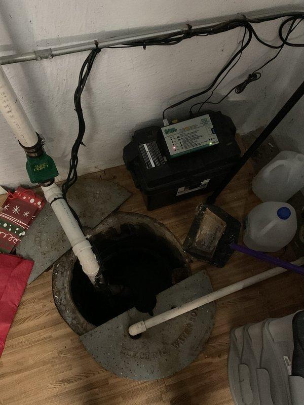 Responded to service call for battery backup sump pump system displaying error code and audible alarm despite recent battery replacement. Upon arrival, performed comprehensive inspection of 6-year-old sump pump installation including primary pump unit, backup battery system, control panel, discharge piping, and sump pit assembly. Examined electrical connections, tested float switch operation, and evaluated PVC discharge line routing and check valve functionality. Inspected battery backup control module mounted on wall, verified cable connections, and assessed monitoring display readings. Documented existing installation configuration including pit location, pump mounting, and associated plumbing components to determine root cause of system malfunction and provide recommendations for repair or replacement.