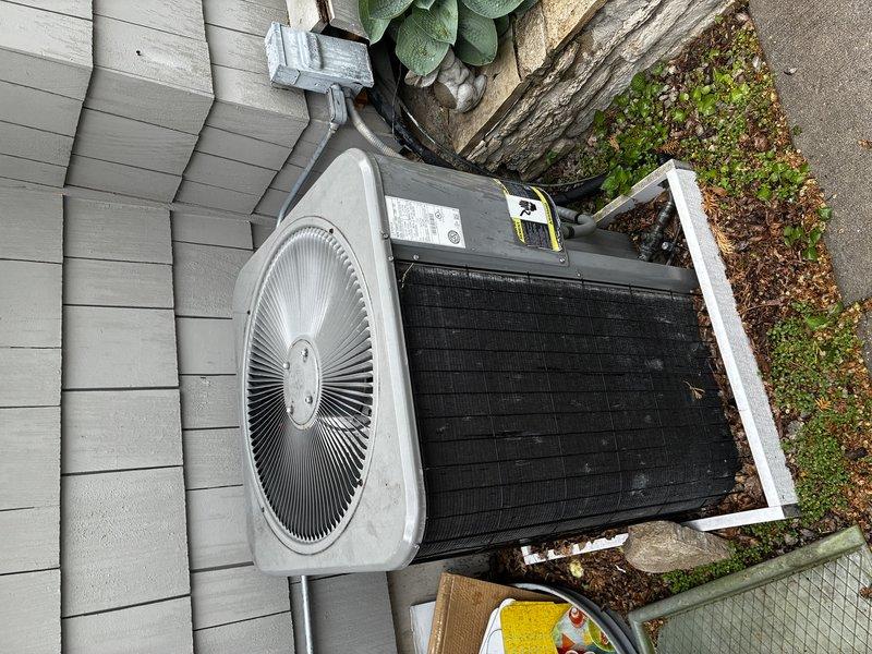 Completed emergency residential AC replacement for 15-year-old failed system. Removed existing outdoor condensing unit and installed new air conditioning system on concrete pad adjacent to building with gray siding. Unit positioned in side yard area with proper clearances maintained from structure and landscaping. Connected electrical conduit to exterior wall and verified all refrigerant lines, electrical connections, and drainage systems functioning properly. System tested and operational upon completion.