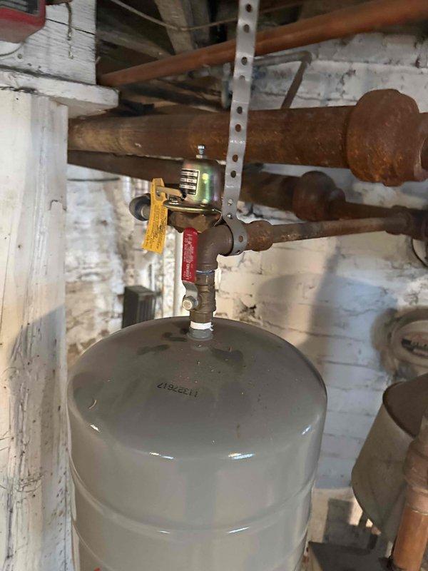 Completed on-site assessment for boiler replacement estimate at residential property. Inspected existing hydronic heating system including aged boiler equipment, pressure tank with brass fittings and red-handled isolation valve, and corroded distribution piping showing significant oxidation. Evaluated Caleffi zone actuator with end switch controlling attic zone, confirmed operational wiring connections, and documented multi-zone heating configuration. Photographed mechanical room infrastructure including exposed joists, white painted brick walls, and deteriorating pipe conditions to determine proper equipment sizing and installation requirements. Provided recommendations for new boiler system replacement based on current heating load, zone control needs, and existing piping layout.