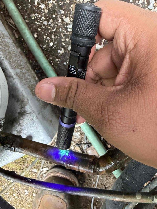 Performed UV leak detection inspection on refrigerant lines using specialized diagnostic equipment. UV tracer dye fluorescence was observed on copper refrigerant piping, confirming leak location. This is a return visit to allow dye settlement time for accurate leak identification, with follow-up scheduled to complete repairs.