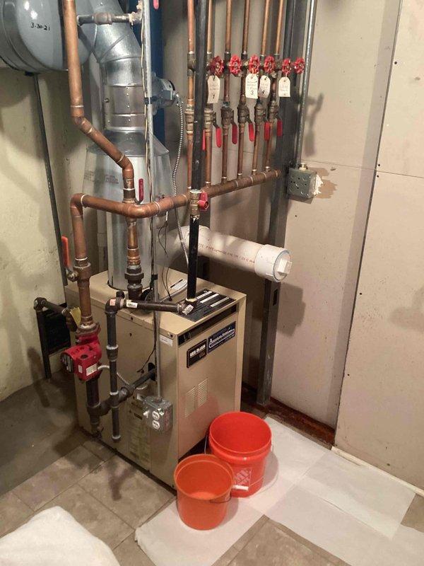 Responded to service call for leaking valves on hydronic heating system. Upon arrival, inspected boiler manifold assembly and associated zone valves in basement mechanical room. Identified multiple leaking spigots on the copper piping manifold with red-handled isolation valves. Tightened packing nuts on affected valve stems and replaced deteriorated valve packing where necessary. Tested all zone valves for proper operation and verified no additional leaks present throughout the system. Placed collection buckets as temporary measure during initial assessment. System restored to normal operation with all leaks eliminated prior to homeowner's scheduled travel.