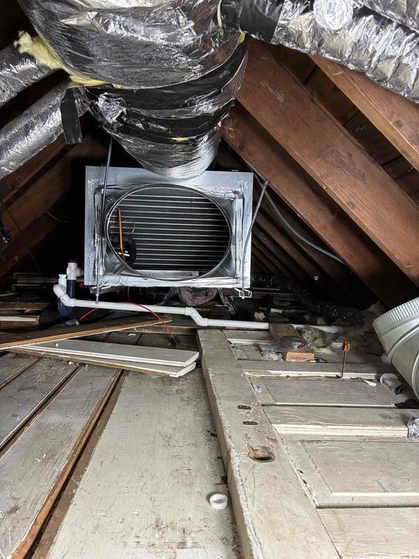 Completed full replacement of residential air conditioning system and Unico high-velocity HVAC system in attic space. Removed existing equipment and installed new evaporator coil unit with horizontal fin heat exchanger, mounted securely to roof structure underside. Connected black flexible insulated ductwork to evaporator unit and secured all runs with appropriate strapping to wooden beams. Installed white PVC condensate drain lines from unit base for proper drainage. Wrapped all ductwork with reflective silver foil-backed insulation to maximize efficiency and prevent heat transfer in attic environment. Routed large flexible metal ductwork throughout attic space following existing pathways, ensuring proper support and connection points. Positioned rectangular HVAC air handler unit on wooden platform with proper clearances for service access. Verified all duct connections are sealed and insulated per manufacturer specifications. Installation required two technicians working full day to 