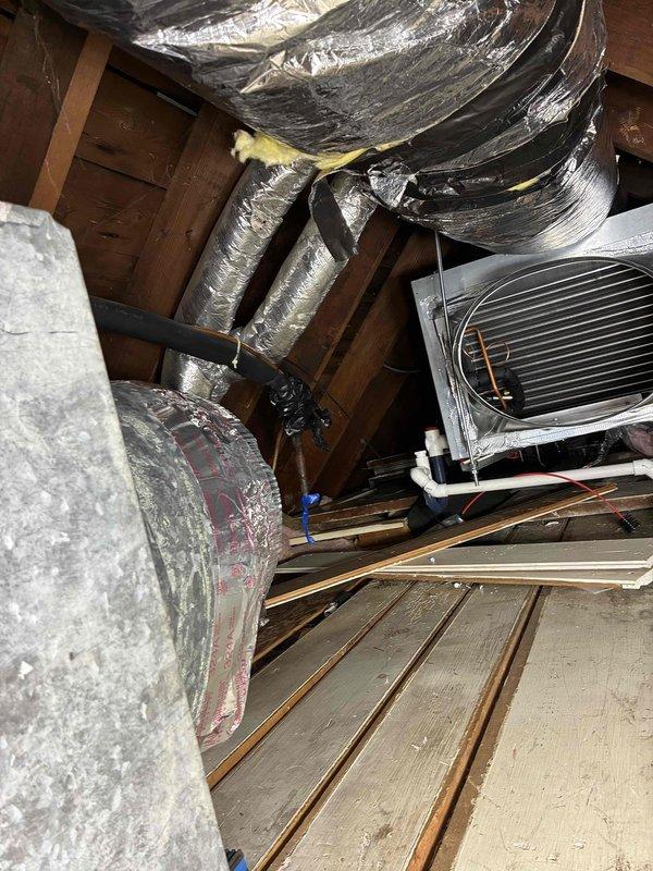 Completed full replacement of residential air conditioning system and Unico high-velocity HVAC system in attic space. Removed existing equipment and installed new evaporator coil unit with horizontal fin heat exchanger, mounted securely to roof structure underside. Connected black flexible insulated ductwork to evaporator unit and secured all runs with appropriate strapping to wooden beams. Installed white PVC condensate drain lines from unit base for proper drainage. Wrapped all ductwork with reflective silver foil-backed insulation to maximize efficiency and prevent heat transfer in attic environment. Routed large flexible metal ductwork throughout attic space following existing pathways, ensuring proper support and connection points. Positioned rectangular HVAC air handler unit on wooden platform with proper clearances for service access. Verified all duct connections are sealed and insulated per manufacturer specifications. Installation required two technicians working full day to 