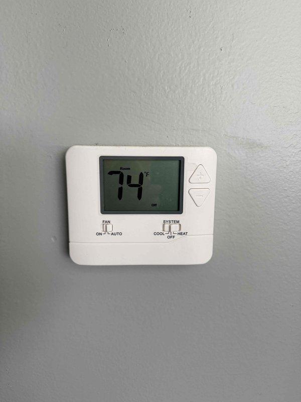 Conducted on-site evaluation for residential two-flat HVAC system replacement. Assessed existing 12-year-old air conditioning unit and documented current thermostat configuration showing digital display set to 74 degrees in OFF mode with AUTO fan setting. Performed measurements of window openings and interior spaces to determine equipment access requirements and confirmed no ladder work necessary for installation. Documented site conditions through photographic records to support equipment sizing and replacement specifications for proposal preparation.