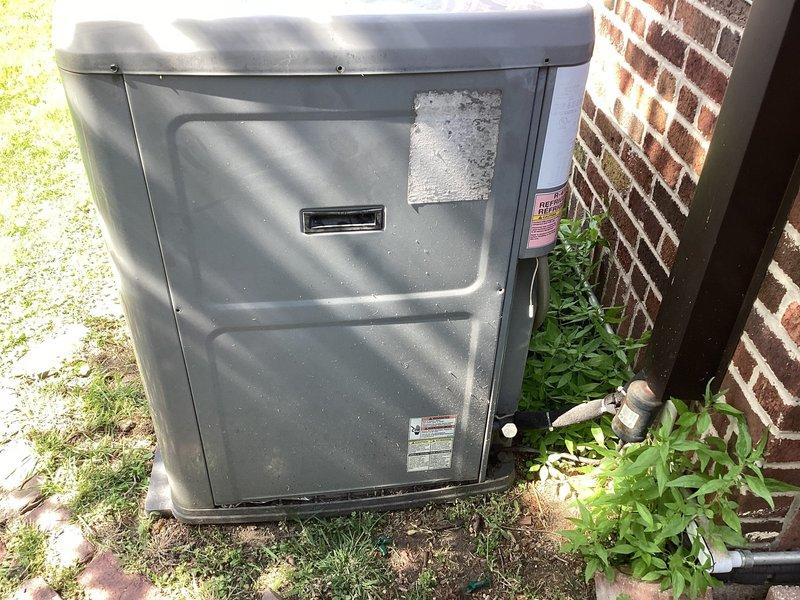 Responded to no cooling complaint on residential air conditioning system. Upon arrival, performed visual inspection of outdoor condensing unit located on ground-level pad adjacent to brick exterior. Unit appeared to be in serviceable condition with normal weathering. Examined condenser cabinet, coil access panels, and ventilation grilles for any obvious signs of mechanical failure or damage. Verified unit identification and specifications from manufacturer nameplate. Documented equipment condition through photographs showing exterior cabinet, top grille assembly, and mounting hardware. Cleared vegetation growth from around unit base to ensure proper airflow and drainage. Assessed condenser fan grille for debris accumulation and verified structural integrity of cabinet panels and fasteners.