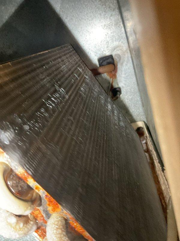 Responded to no airflow complaint on aging air conditioning system. Upon inspection, found evaporator coil completely frozen with heavy ice accumulation, restricting all airflow through the unit. Documented frozen coil condition showing significant frost buildup across aluminum fins and refrigerant lines. System shutdown was necessary to allow complete defrost cycle before further diagnosis could determine root cause, which typically indicates restricted airflow from dirty filter, low refrigerant charge, or failed blower motor components.