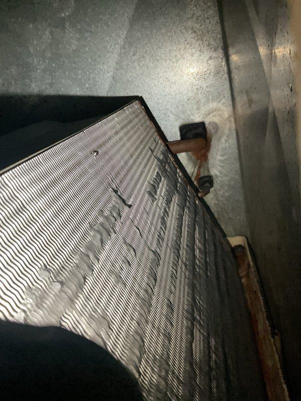 Responded to no airflow complaint on aging air conditioning system. Upon inspection, found evaporator coil completely frozen with heavy ice accumulation, restricting all airflow through the unit. Documented frozen coil condition showing significant frost buildup across aluminum fins and refrigerant lines. System shutdown was necessary to allow complete defrost cycle before further diagnosis could determine root cause, which typically indicates restricted airflow from dirty filter, low refrigerant charge, or failed blower motor components.