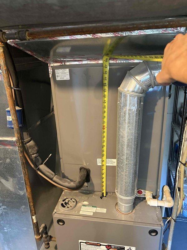 Conducted on-site assessment of existing HVAC system for replacement estimate. The current air conditioning and heating unit, estimated to be 10-15 years old, was thoroughly evaluated in the basement utility area. Performed detailed measurements of the existing gray metal furnace/air handler cabinet to determine spatial requirements and clearances for potential replacement equipment. Documented vertical dimensions of the main unit and assessed the current ductwork configuration, including the cylindrical silver metallic supply duct with elbow connection to horizontal distribution system. Examined associated plumbing infrastructure, including copper refrigerant lines and condensate drainage components. Measured clearance beneath related plumbing fixtures to verify adequate space for new equipment installation. Photographed existing system components, manufacturer specification labels, electrical conduit routing, and mechanical connections to provide accurate documentation for replacemen