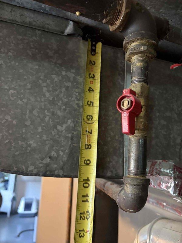 Conducted on-site assessment of existing HVAC system for replacement estimate. The current air conditioning and heating unit, estimated to be 10-15 years old, was thoroughly evaluated in the basement utility area. Performed detailed measurements of the existing gray metal furnace/air handler cabinet to determine spatial requirements and clearances for potential replacement equipment. Documented vertical dimensions of the main unit and assessed the current ductwork configuration, including the cylindrical silver metallic supply duct with elbow connection to horizontal distribution system. Examined associated plumbing infrastructure, including copper refrigerant lines and condensate drainage components. Measured clearance beneath related plumbing fixtures to verify adequate space for new equipment installation. Photographed existing system components, manufacturer specification labels, electrical conduit routing, and mechanical connections to provide accurate documentation for replacemen