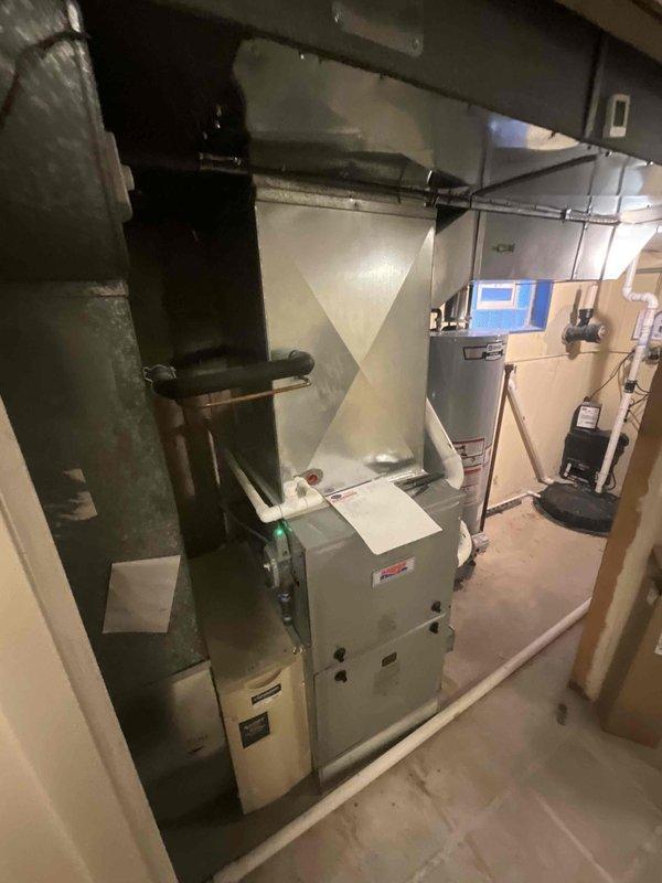 Conducted comprehensive assessment of existing residential HVAC system located in basement utility area for full system replacement quote. Evaluated current furnace unit, ductwork configuration including galvanized metal plenum and flexible ducting sections, condensate pump assembly with PVC drainage lines, and overall mechanical room layout. Documented equipment condition showing age-related wear, dust accumulation on duct components, and existing installation configuration with water heater proximity. Photographed complete system setup to provide detailed visual reference for replacement specifications and equipment sizing requirements.