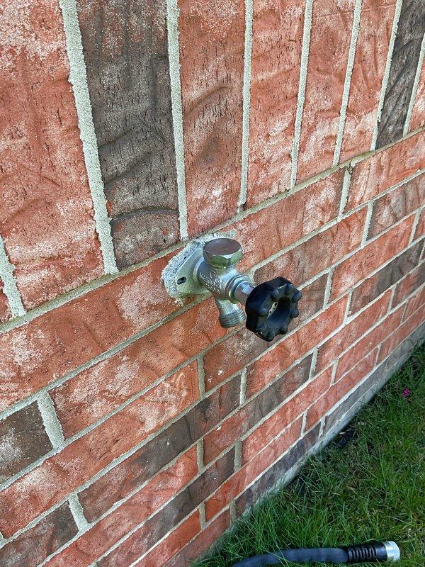 Responded to a low water pressure complaint at an outdoor ground-level spigot on a 16-year-old home. Upon inspection, found the existing hose bib mounted to the exterior brick wall showing signs of age and potential internal deterioration affecting flow rate. Evaluated the spigot assembly, including the valve body and connection integrity, and documented the condition with photographs. Also inspected interior plumbing connections beneath bathroom sink to rule out supply line issues affecting overall household water pressure.