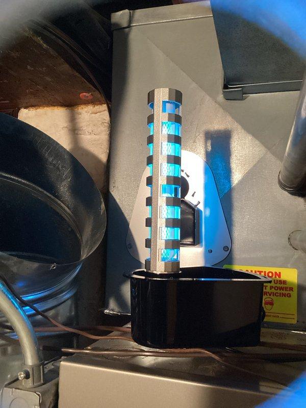 Returned to complete installation of replacement REME HALO UV bulb in existing air purification system. Removed old UV bulb from mounted housing unit within the HVAC system and installed new bulb with characteristic blue ionization element. Verified proper mounting and secure connection to black circular base housing. System tested and confirmed operational upon completion.
