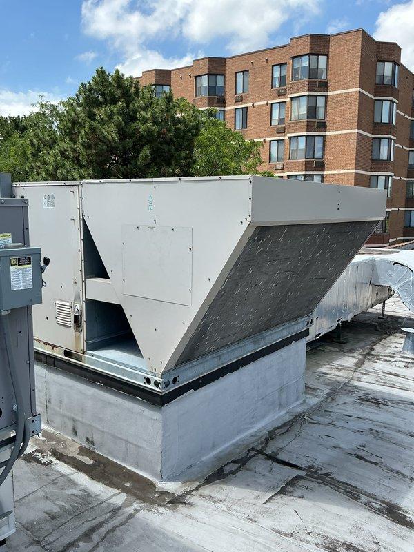 Performed inspection of rooftop unit serving theater space to assess serviceability and determine refrigerant type for potential maintenance agreement enrollment. Accessed RTU on flat membrane roof using telescopic ladder, documented thermostat location and current settings showing 67°F in cooling mode, and photographed equipment specifications including refrigerant data plate information. Confirmed unit is serviceable and provided recommendations for ongoing maintenance program eligibility.