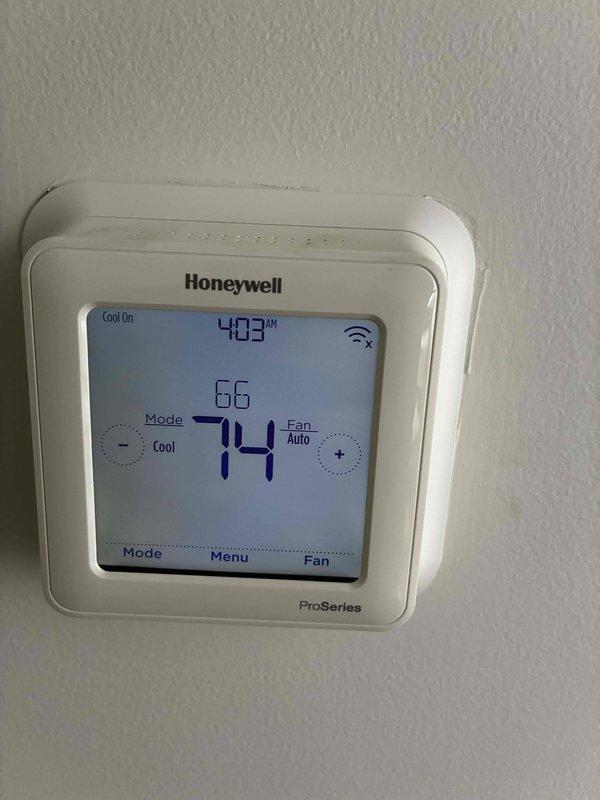 Responded to service call for upstairs air conditioning system not cooling properly, an ongoing issue with a six-year-old unit. Upon arrival, inspected the Honeywell ProSeries thermostat which displayed system operating in cooling mode with a setpoint of 74°F and current temperature reading of 66°F at time of inspection. Accessed the air handler unit and observed significant moisture accumulation and condensation throughout the interior compartment, with water droplets visible on metal surfaces and evidence of corrosion staining along seams and panel edges. Examined the refrigerant lines, blower motor housing, and internal components. Documented system conditions with photographs showing excessive moisture presence within the unit, which indicates potential drainage issues, airflow restrictions, or refrigerant system problems requiring further diagnosis and repair to restore proper cooling function and prevent continued moisture-related damage to the equipment.