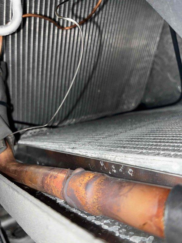Responded to callback for newly installed AC system not maintaining temperature below 80°F. Upon inspection, discovered severely corroded copper refrigerant line at evaporator coil with visible rust and oxidation damage. Identified improper installation practices from recent system replacement, including compromised refrigerant piping and potential leak points affecting system performance. Documented conditions with photos showing corroded copper line, evaporator coil assembly, and drain pan area. Recommended immediate refrigerant line replacement and system leak testing to restore proper cooling capacity.