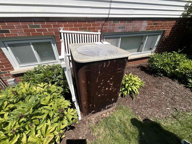 Completed comprehensive replacement estimate for residential air conditioning system. Existing system utilizes R22 refrigerant and is over 15 years old, with outdoor condensing unit positioned at ground level showing significant rust and weathering on protective enclosure, and indoor air handler/furnace located in basement utility area with vertical ductwork configuration. Assessed equipment condition, measured installation parameters, documented current system layout including refrigerant line routing and electrical connections, and photographed both indoor and outdoor components to provide accurate replacement specifications and pricing options for modern high-efficiency equipment upgrade.