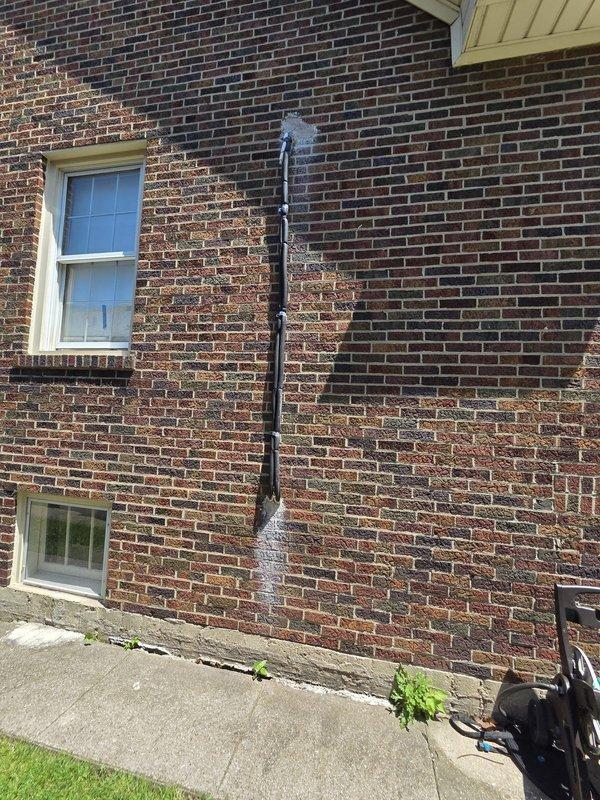 Returned to property to address exterior wall penetration from previous HVAC installation. Patched hole in brick wall where condensate drain line passes through exterior surface. Verified proper sealing around black corrugated drainage pipe and white PVC elbow fitting to prevent water intrusion and maintain building envelope integrity. Documented completed work with photos showing vertical drain line installation along brick facade and proper connection of drainage components.