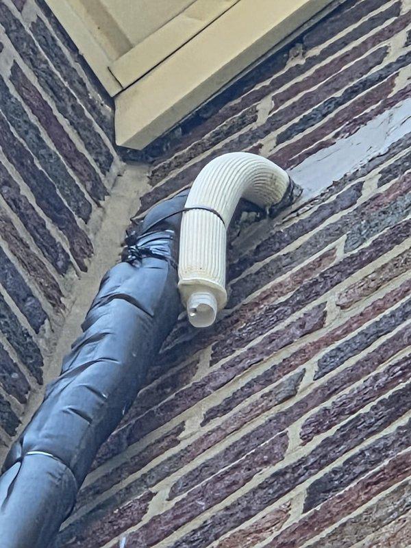 Returned to property to address exterior wall penetration from previous HVAC installation. Patched hole in brick wall where condensate drain line passes through exterior surface. Verified proper sealing around black corrugated drainage pipe and white PVC elbow fitting to prevent water intrusion and maintain building envelope integrity. Documented completed work with photos showing vertical drain line installation along brick facade and proper connection of drainage components.