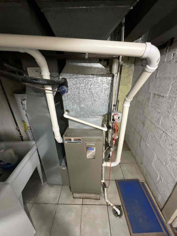 Replaced 20-year-old residential air conditioning system and 18-year-old furnace due to failed evaporator coil and complete refrigerant loss in obsolete R22 system. New HVAC equipment installed in basement mechanical room with updated condensate drainage system and exterior condenser unit positioned against brick exterior wall with proper electrical disconnect and refrigerant line routing.