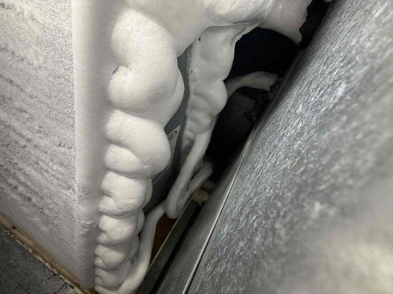 Responded to no cooling complaint on 10+ year old AC system. Upon inspection, found significant ice accumulation on refrigerant lines and insulation in indoor unit area, indicating restricted airflow or low refrigerant charge. System was making abnormal noise during operation. Inspected outdoor condensing unit and verified proper drainage system operation with PVC condensate lines functioning as designed. Heavy frost buildup on suction line confirmed cooling system malfunction requiring immediate attention to prevent compressor damage.
