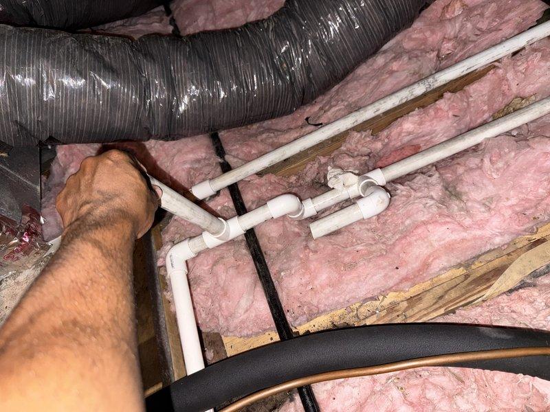 Responded to callback for newly installed AC unit not cooling properly. Upon inspection, verified return air grille installation and traced ductwork and condensate drain lines in attic space. Examined PVC condensate piping connections and flexible ductwork routing between joists. System components appeared properly installed with adequate insulation coverage around ductwork. Identified and resolved cooling issue, confirmed unit operating to manufacturer specifications before departure.