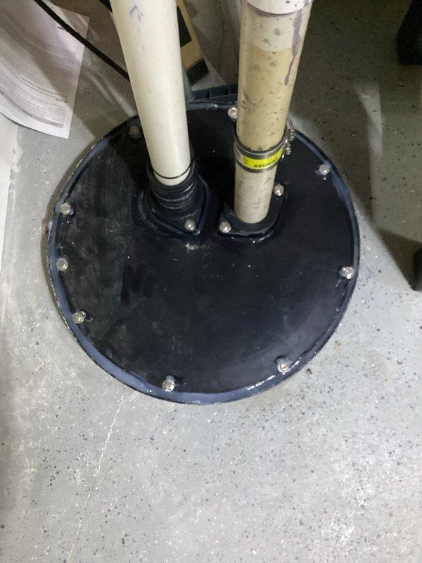 Responded to callback for sewage ejector pump installation experiencing odor issues. Inspected floor seal assembly and pipe penetrations through concrete floor. Verified proper seating of rubber boot seal around dual PVC discharge pipes and confirmed all perimeter bolts were properly torqued to prevent sewer gas escape from pit.