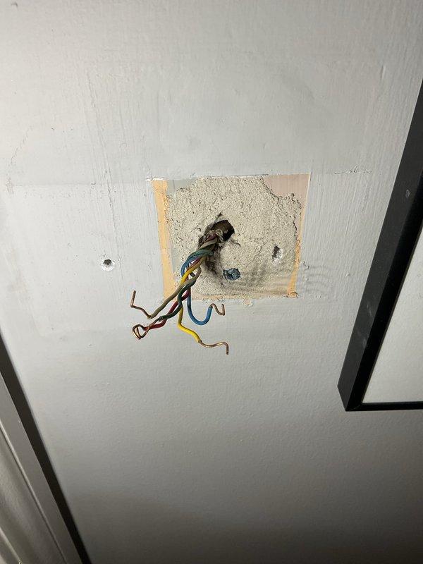 Responded to warranty call for non-operational thermostat following recent AC installation. Upon arrival, found thermostat completely removed from wall with exposed wiring at ceiling location. Documented existing conditions showing brown, blue, and yellow/green striped wires protruding from opening with visible drywall patching around fixture area. Inspected HVAC system in mechanical room, verifying furnace and ductwork connections were intact. Photographed equipment layout including condensation on vertical duct run. Thermostat requires replacement to restore system operation.