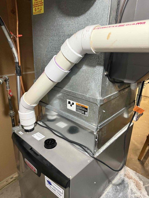 Conducted comprehensive assessment of existing HVAC system for full replacement estimate with primary focus on air conditioning components. Evaluated current furnace/air handler unit, ductwork configuration, and associated mechanical systems including humidifier, ventilation piping, and refrigerant lines. Documented system layout showing gray metal air handler with PVC exhaust venting, copper refrigerant piping, flexible and rigid ductwork connections, and electrical service. Photographed equipment specifications, manufacturer labels, and current installation configuration to provide accurate sizing and replacement recommendations for complete system upgrade.