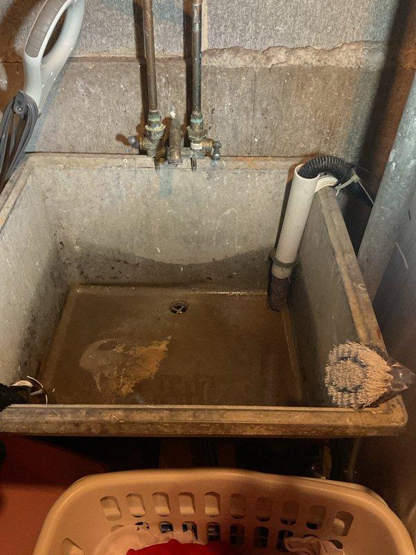 Completed comprehensive plumbing inspection of residential property. Evaluated utility sink installation in basement area, documenting aging concrete basin with significant mineral staining and copper supply lines with shutoff valves showing normal wear. Inspected drainage system, water filtration components, and vertical PVC waste stack with proper mounting brackets. All plumbing systems photographed and assessed for current condition and functionality.