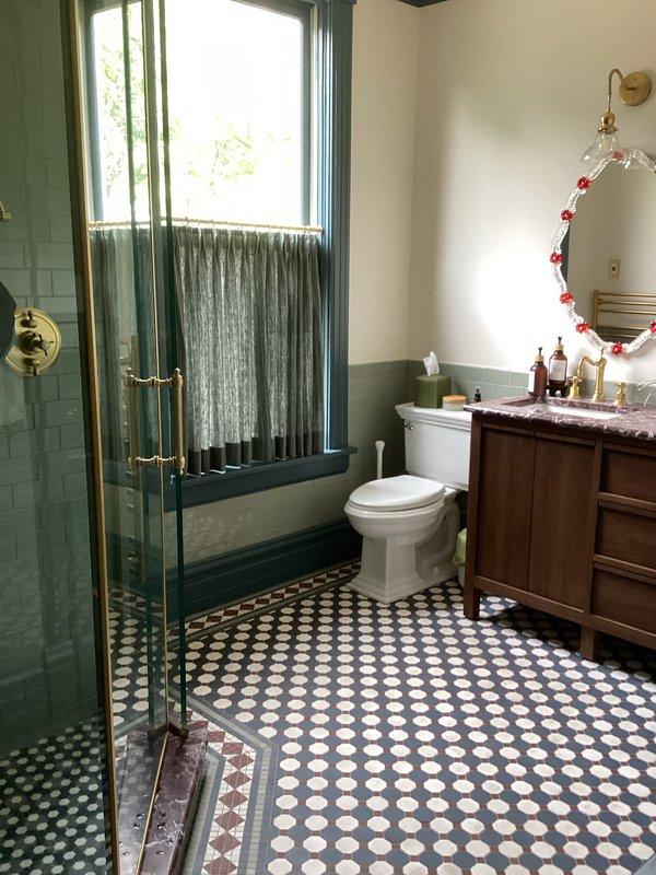 Completed comprehensive plumbing inspection of residential property, examining two full bathrooms for proper fixture operation, drainage, and potential issues. Inspected modern walk-in shower with glass enclosure, verifying chrome handheld showerhead functionality, sliding rail mounting, shower controls operation, and proper drainage through floor-mounted square drain; confirmed subway tile and mosaic accent installations showed no signs of water intrusion or grout deterioration. Evaluated second bathroom featuring vintage-style fixtures with brass/gold-toned components, including shower enclosure with glass doors and brass hardware, toilet operation, and wooden vanity with marble countertop and gold-toned faucet; verified all fixtures operated correctly with adequate water pressure and proper drainage throughout both bathrooms with no leaks detected.