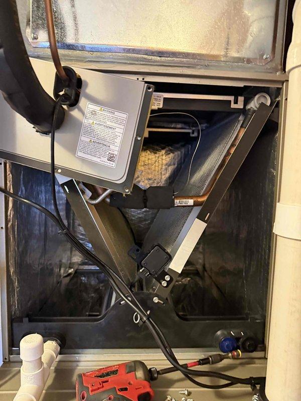 Responded to callback for non-operational HVAC unit with water accumulation following recent water safety device installation. Upon inspection, identified active condensate leak causing water to collect in bucket. Accessed interior unit compartment and crawl space area to trace leak source along condensate drain line and PVC piping connections. Examined water safety device installation, drain pan, and associated plumbing components. Documented conditions with photos showing unit interior, drain components, and crawl space piping layout for diagnostic purposes and repair verification.